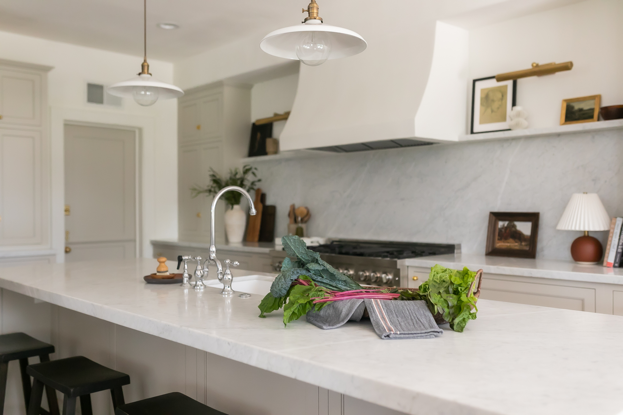 Marble kitchen island with fresh vegetables and brass pendants — J. Arthur Custom Homes, Texas Hill Country