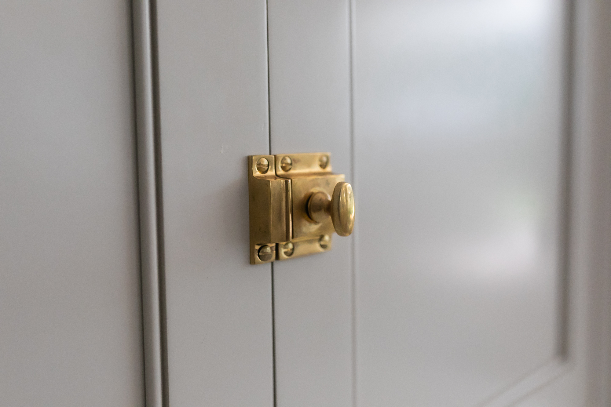 Custom brass cabinet latch on gray shaker door — J. Arthur Custom Homes finish detail