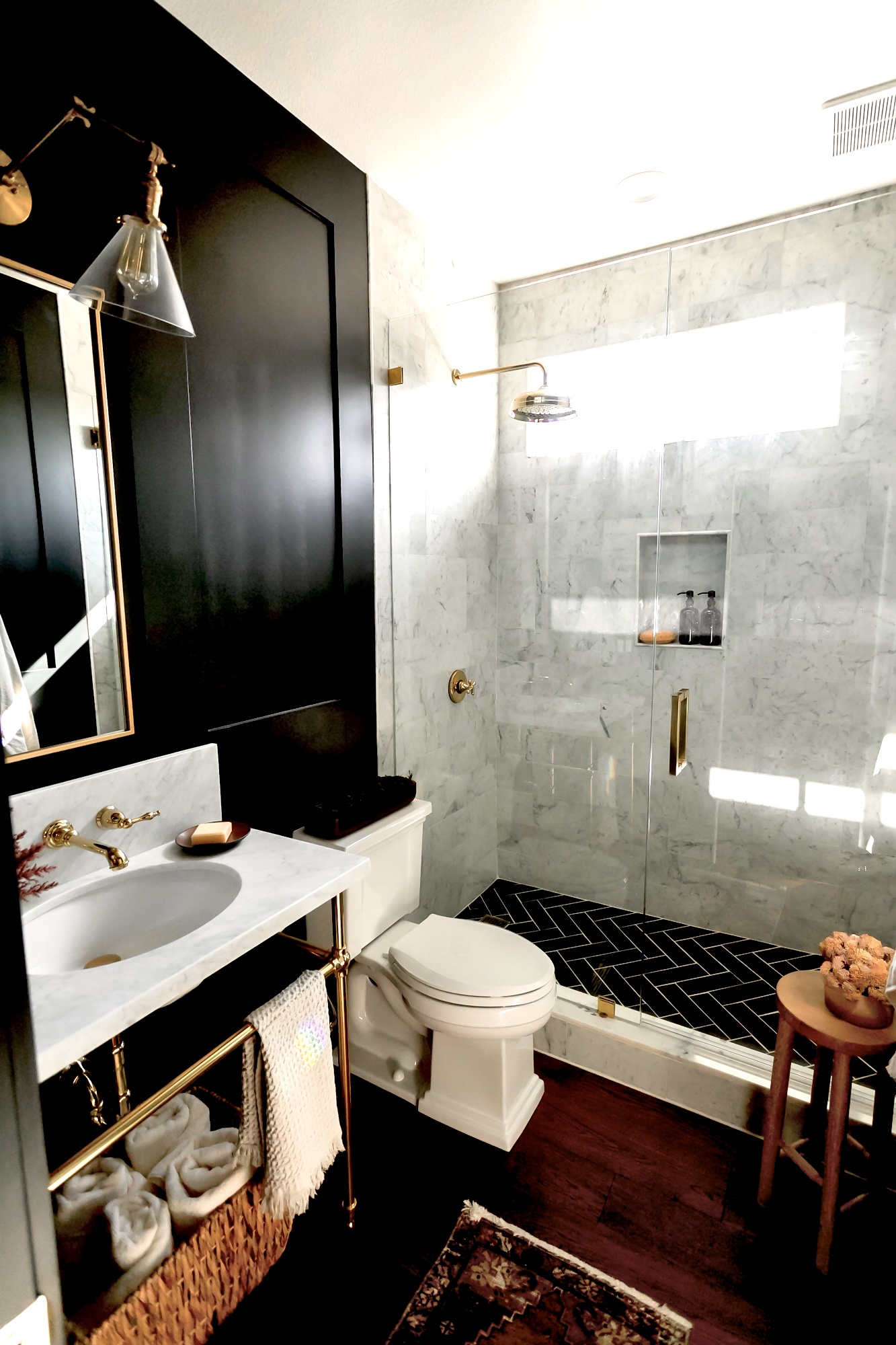 Black bathroom with marble shower, brass rain head, and herringbone tile floor — J. Arthur Custom Homes